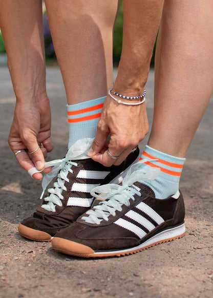 Person, die schwarze Turnschuhe bindet, trägt J.Clay Orange Neon Stripes - Sneaker Socken High mit Blau.