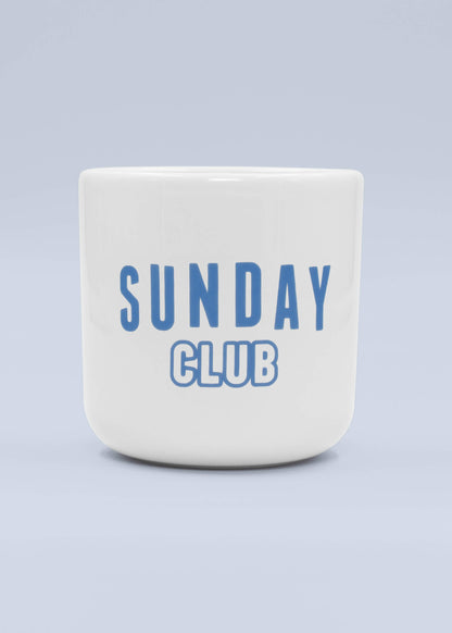 Eine weiße J.Clay Tasse ohne Henkel aus Keramik mit blauem SUNDAY CLUB-Schriftzug auf der Vorderseite und hellblauem Hintergrund - ein ideales Geschenk und eine stilvolle Ergänzung für jedes Geschenkset.