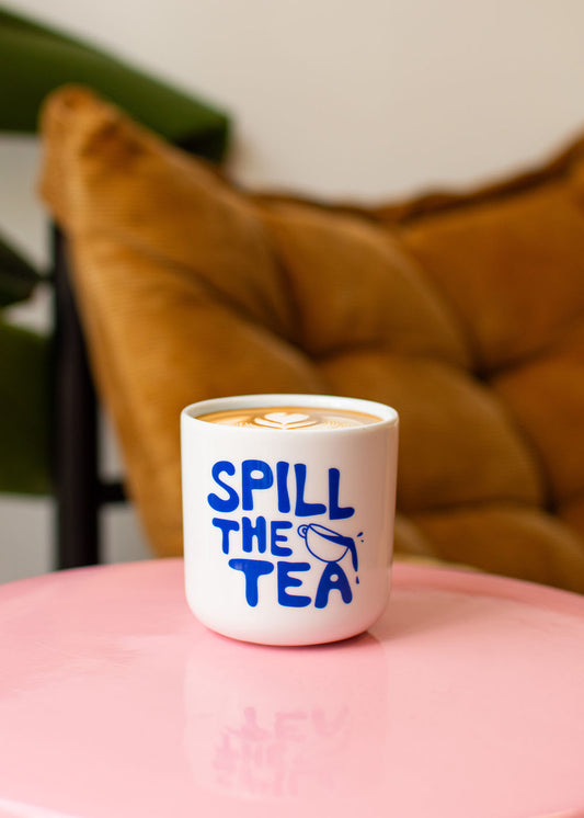 J.Clay „Spill the Tea“ – Tasse mit modernem Design auf einem rosa Tisch, einem hellbraunen Kissen und einer grünen Pflanze.