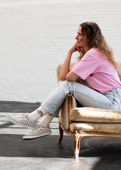 Eine Frau in einem rosa Shirt, J.Clay „I don’t care“-Tennissocken und Jeans sitzt seitlich auf einem Vintage-Sofa.