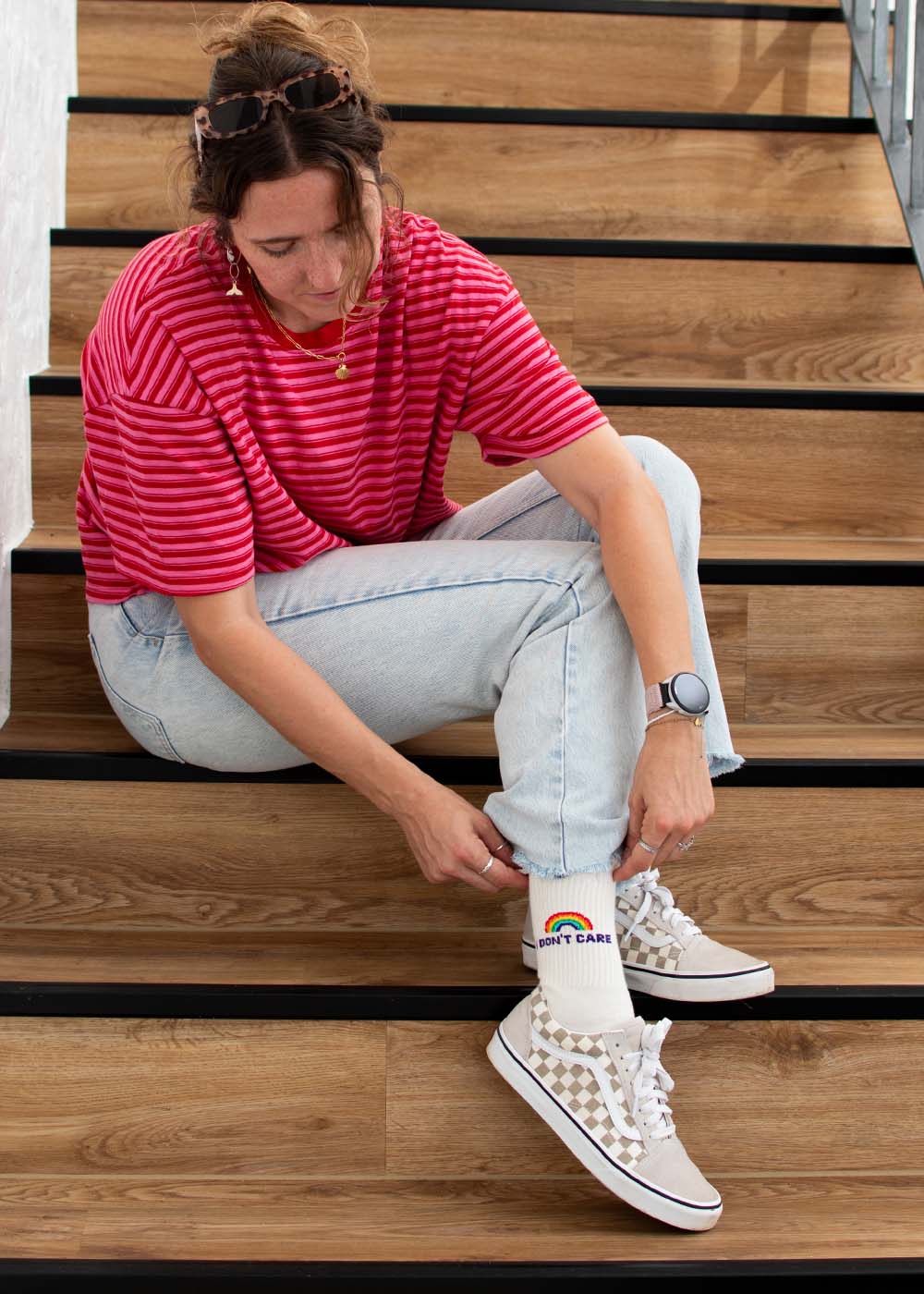 Eine Frau zieht J.Clay „I don’t care“-Tennissocken mit Regenbogenmuster an – ideal für coole Streetstyle-Looks.