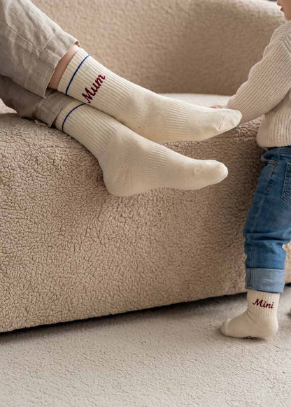 Erwachsener und Kind in J.Clay Mini Mum - Fam Pack cremefarbene Socken neben einem Sofa.
