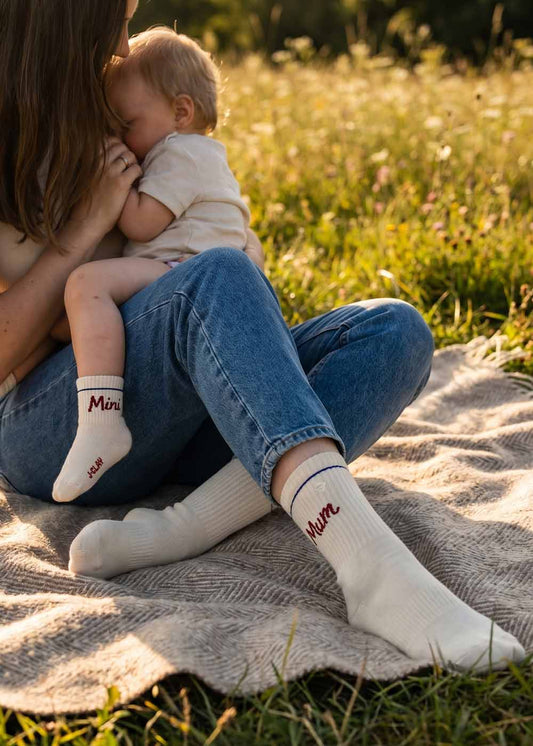 Eine Mutter kuschelt im Freien mit ihrem Baby, beide tragen passende J.Clay Mini Mum - Fam Pack Socken.
