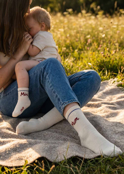 Eine Mutter kuschelt im Freien mit ihrem Baby, beide tragen passende J.Clay Mini Mum - Fam Pack Socken.