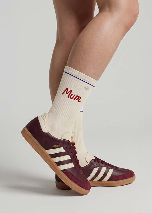 Beine in cremefarbenen Socken von J.Clay Mum und kastanienbraunen Adidas Samba Sneakers mit weißen Streifen.