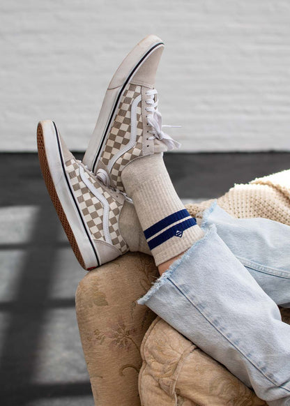 Person in heller Jeans, J.Clay True Stone Navy Tennissocken, karierte Vans, die Beine übereinandergeschlagen.