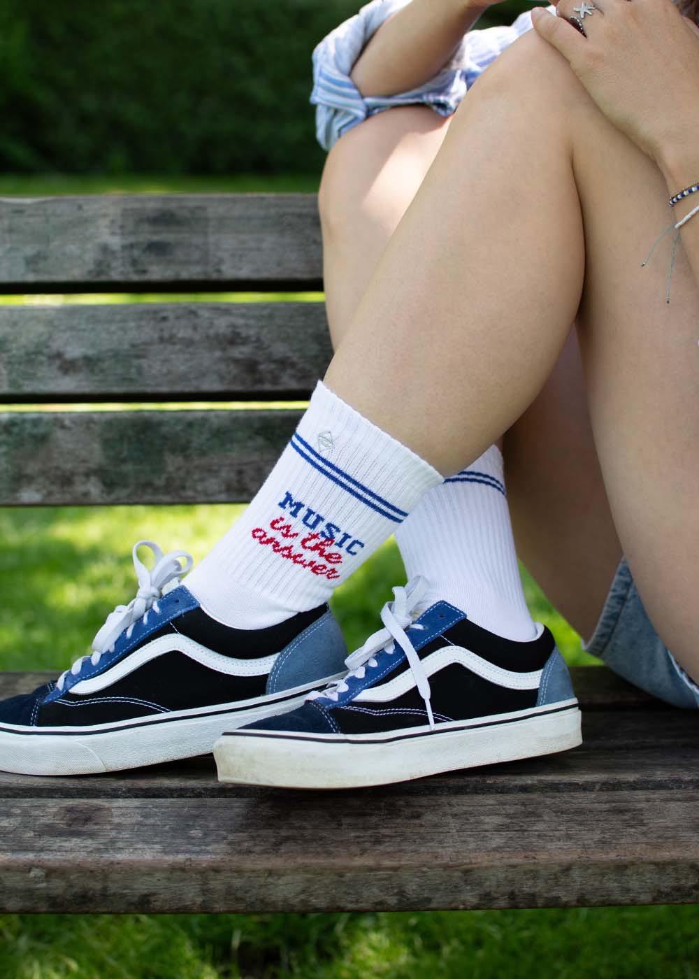Person auf einer Bank in J.Clay Tennissocken, Vans, mit der Aufschrift "Musik ist die Antwort".