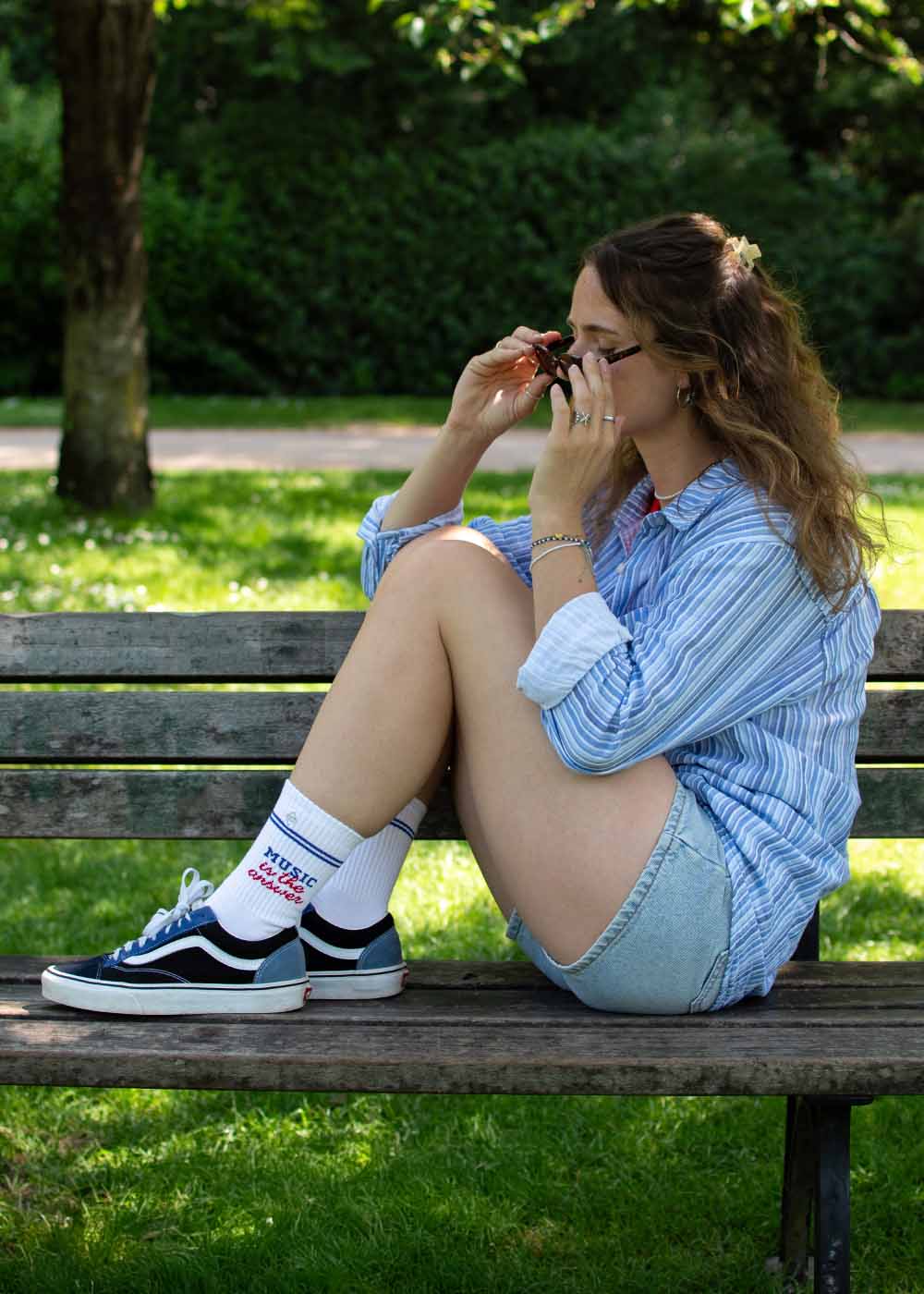 Frau in J.Clays "Music is the answer"-Shirt und Tennissocken auf einer Parkbank, Retro-Vibe.