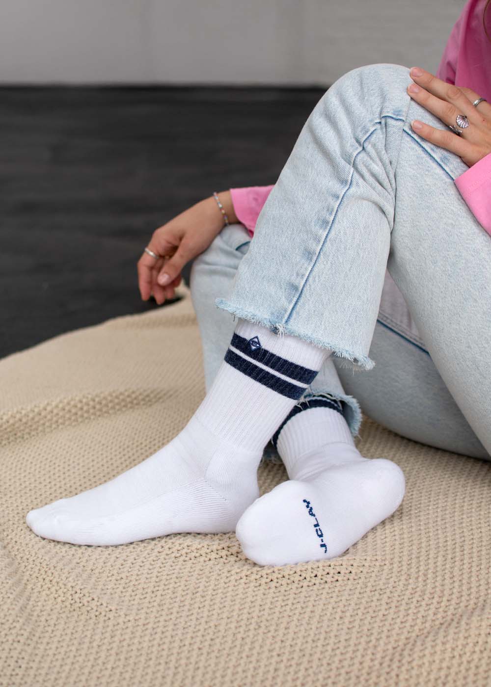 Person in „True Snow Denim“ – Tennissocken von J.Clay, sitzend auf einer beigen, strukturierten Matte.