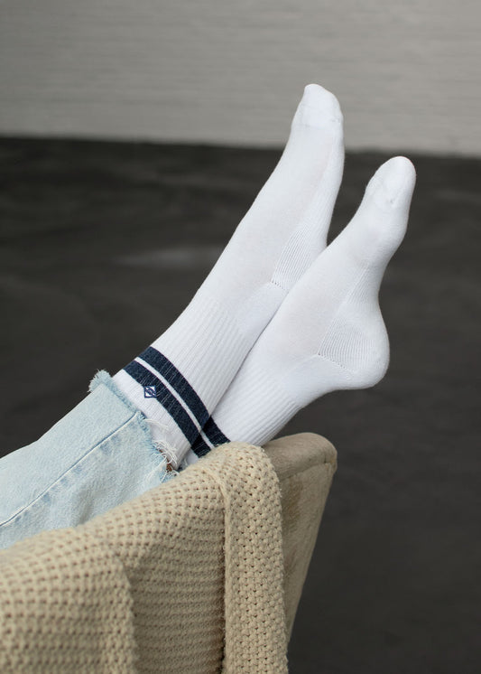 J.Clay True Snow Denim-Tennissocken mit blauen Streifen auf einer beigen Decke und einem hellen Stuhl.