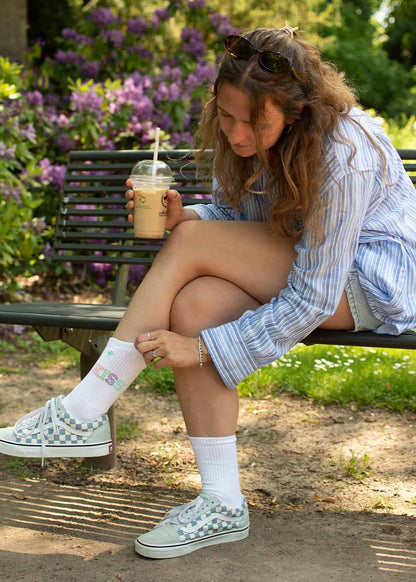 Frau auf einer Bank, die ihre J.Clay Kiss-Socken bewundert, während sie ein eisgekühltes Getränk in der Sonne schlürft.