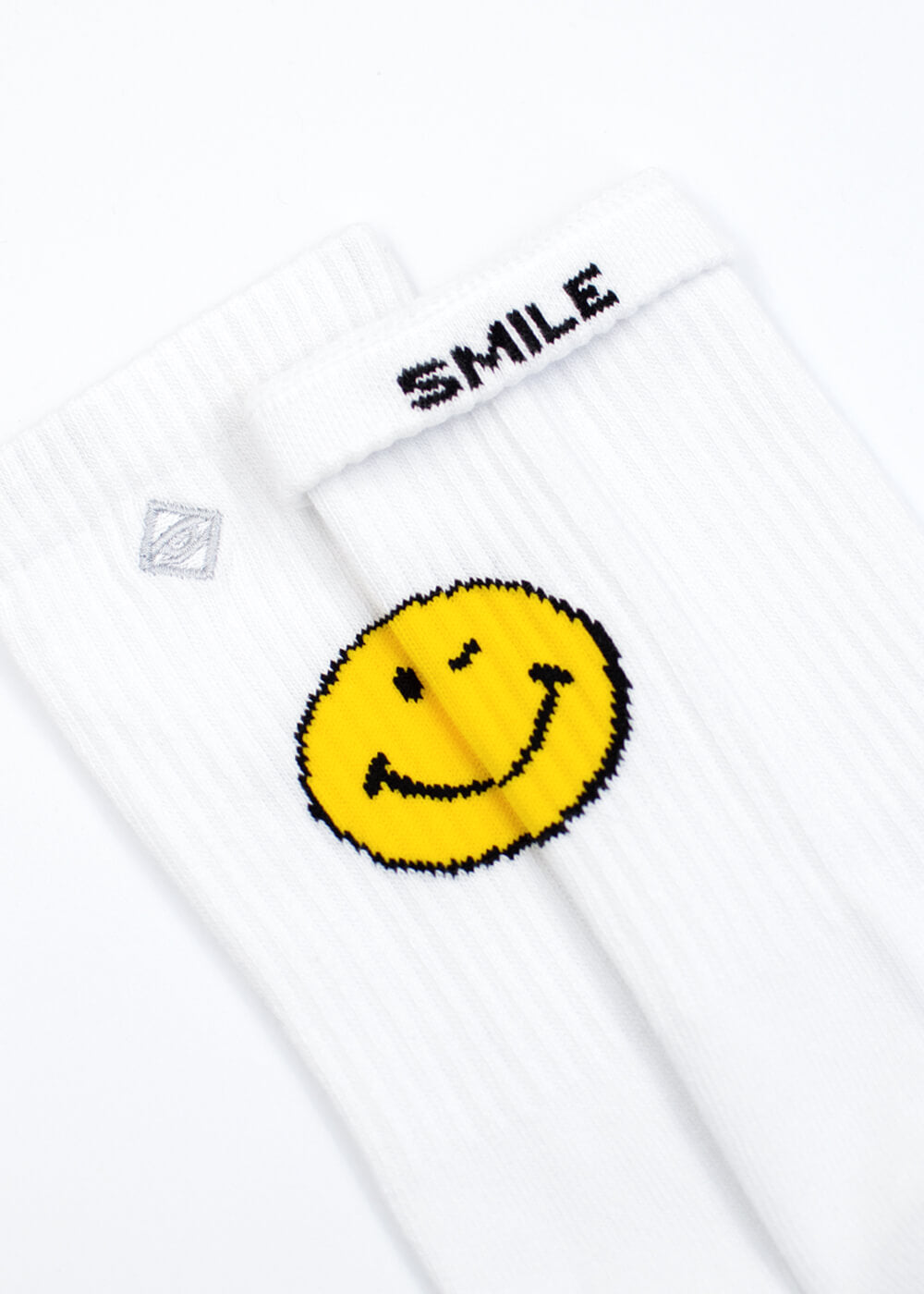 Gelbes Lächeln von J.Clay: Weiße gerippte Tennissocken mit einem großen gelben Smiley-Gesicht und "SMILE" in Schwarz am oberen Bündchen. In Deutschland entworfen und flach auf weißem Hintergrund abgebildet.