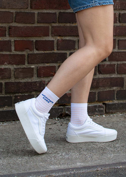 Eine Person in J.Clay’s – immer zu spät – mit Midi und weißen Sneakers geht an einer Backsteinmauer vorbei.
