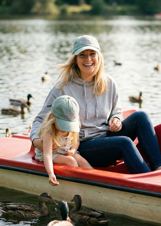 Lächelnde Frau und Mädchen in J.Clay Favourite Child Cap füttern Enten aus einem roten Boot auf dem See.