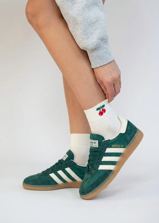 Person trägt grüne Adidas Turnschuhe und J.Clay Cherry - Sneaker Socken High mit Kirschenmotiv.