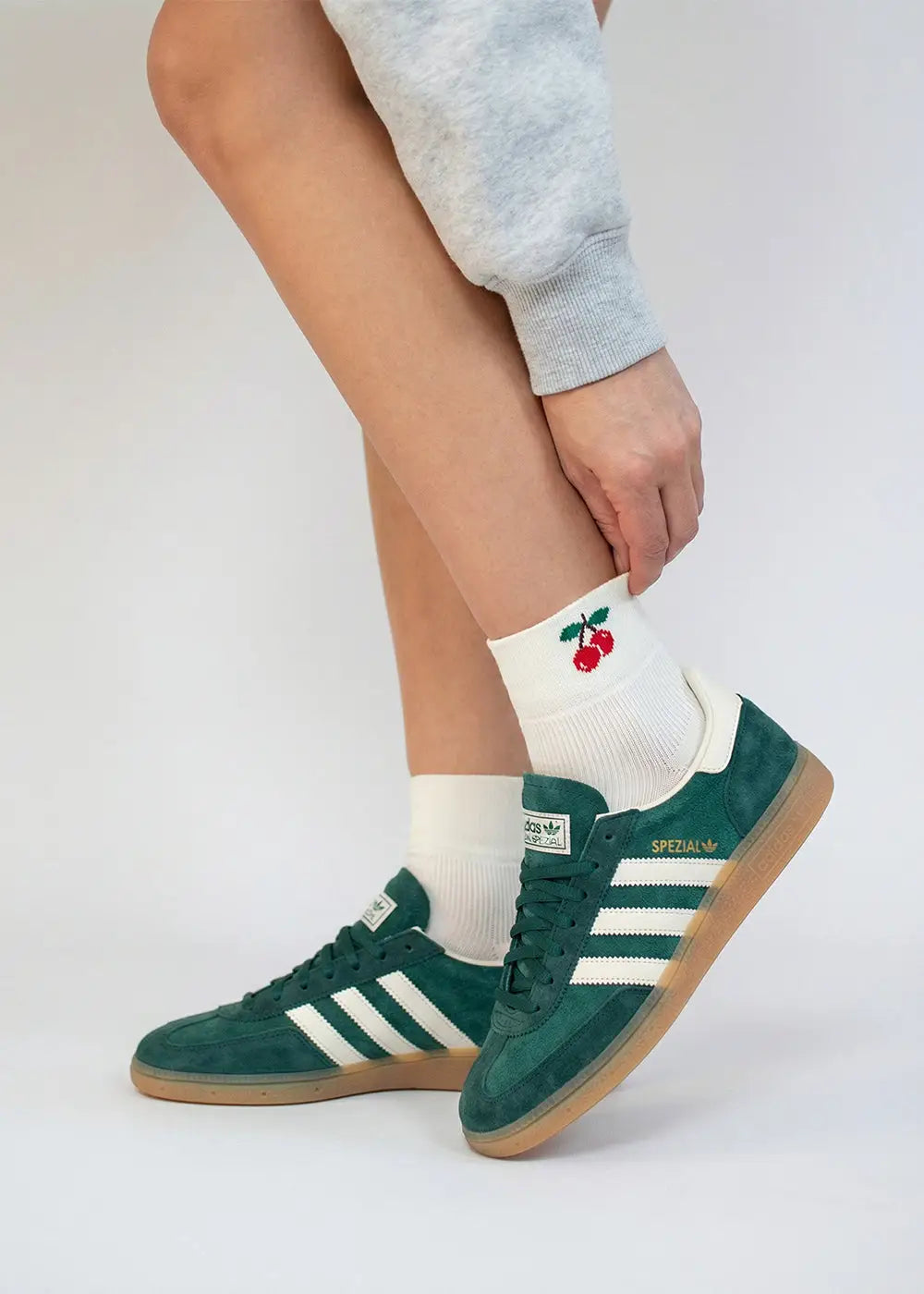 Person trägt grüne Adidas Turnschuhe und J.Clay Cherry - Sneaker Socken High mit Kirschenmotiv.