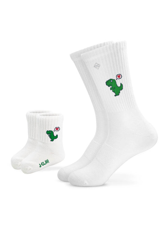 Zwei Paar weiße gerippte J.Clay Mini Me Socken - ein Paar für Erwachsene, ein Paar für Kinder - jeweils mit einem grünen Dinosaurier und einem kleinen roten Herz. Das Kinderpaar hat einen grünen Sohlentext. Perfekt für einen süßen Partner-Look!.