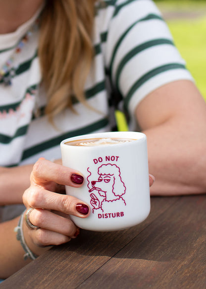Eine Frau hält eine Tasse von J.Clay mit der Aufschrift „Do not Disturb“ und einer Pudel-Illustration in der Hand.