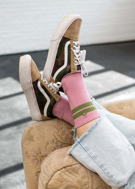 Eine Person trägt „True Rose Olive“-Tennissocken von J.Clay zu Jeans, die Füße auf einem beigen Sofa.
