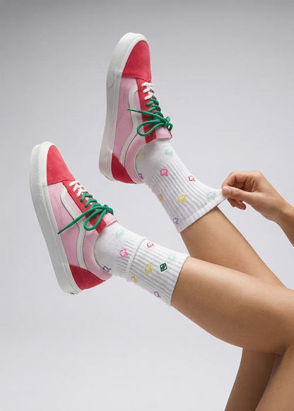 Person trägt J.Clay "Have a nice day" rosa Turnschuhe und weiße Socken mit bunten Symbolen.