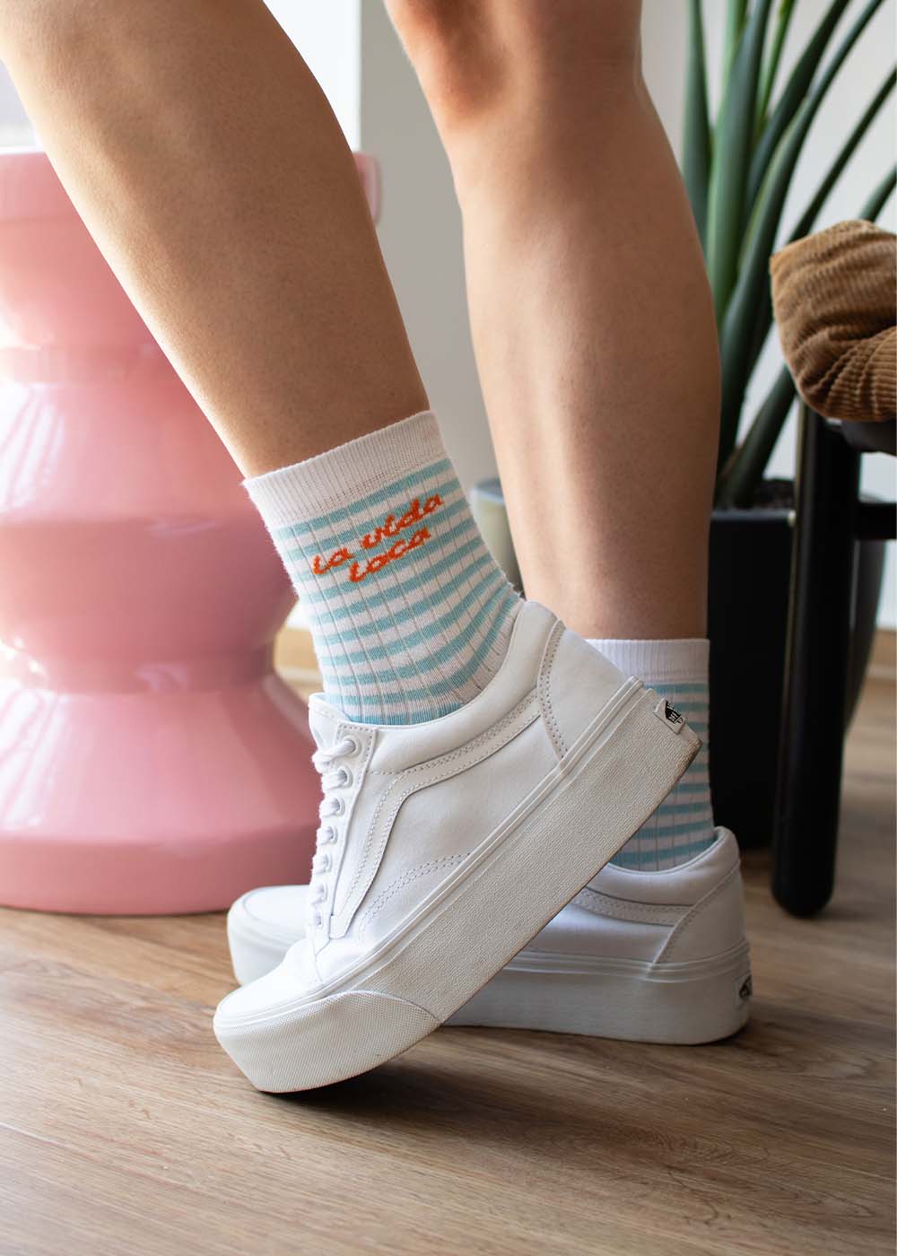Person, die J.Clay „la vida loca“ – blau karierte Midi-Socken trägt und in weißen Sneakers in einem Innenraum steht.