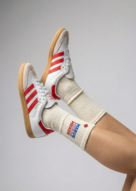 Person trägt Merde Merde-weiße und rote Adidas-Turnschuhe mit J.Clay Tennissocken.