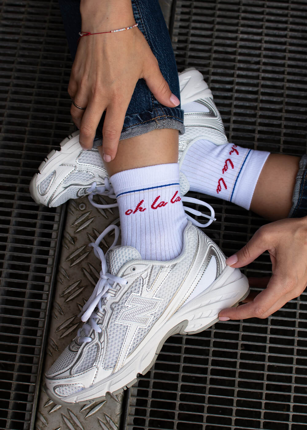 Eine Person, die J.Clay Damen Socken-weiße Baumwollsocken mit rotem "oh la la"-Text- trägt, sitzt auf einem Metallgitter und richtet ihre Hose.