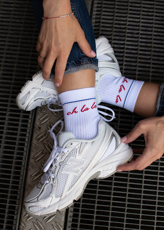 Ein Paar weiße Damen Socken von J.Clay aus weichem Baumwollmaterial mit Rippenstruktur, dünnem blauen Streifen am Bündchen und roter "oh la la"-Stickerei an den Seiten. - Halbhohe Socken für Frauen