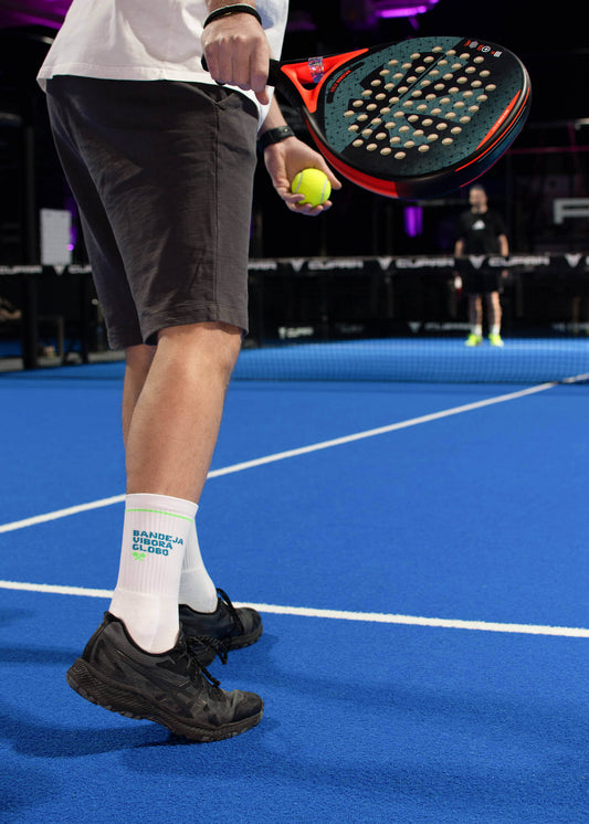 Abgebildet sind zwei weiße J.Clay-Socken mit grünen Akzenten und blauem "BANDEJA UNDERA GLOBO"-Schriftzug, ideal für Padel-Tennis-Fans. Das X SPORTS-Logo in Blau und Weiß ist in der oberen rechten Ecke abgebildet.
