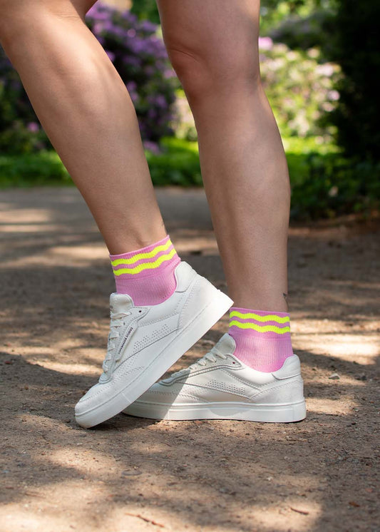 Person trägt J.Clay Neon Wave Sneaker Socken High mit gelben Streifen und weißen Sneakers im Freien.
