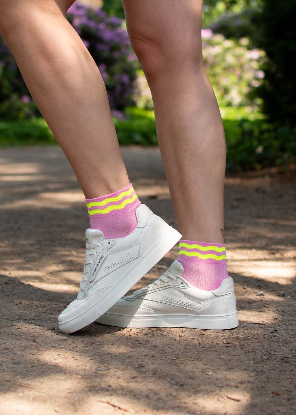Person trägt J.Clay Neon Wave Sneaker Socken High mit gelben Streifen und weißen Sneakers im Freien.