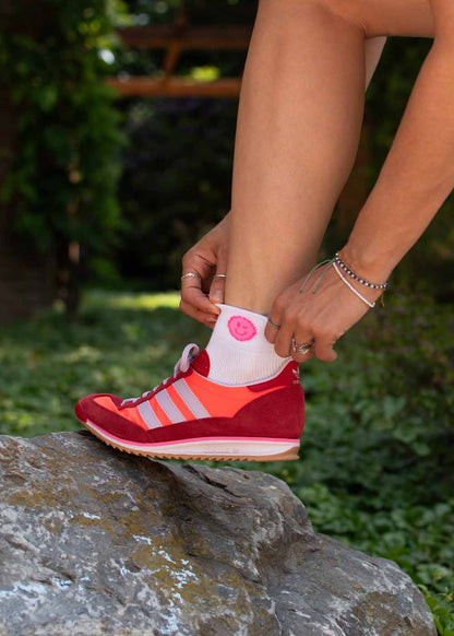 Die Person, die rote Turnschuhe trägt, stellt die J.Clay Neon Smile - Sneaker Socken High auf einem Felsen ein.