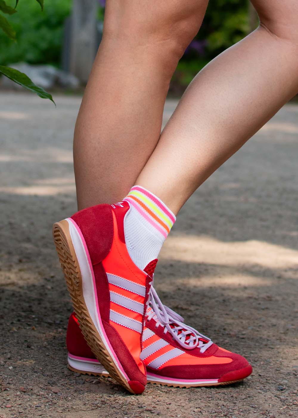 Person mit roten Adidas-Turnschuhen und J.Clay Multi Stripes Neon Sneaker Socken steht draußen.