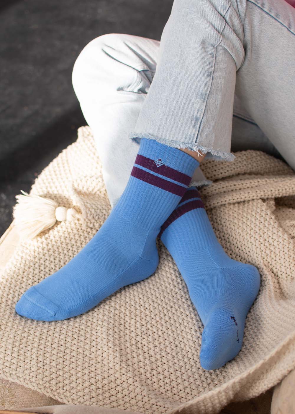 Eine Person trägt J.Clay True Sky Grape – Tennissocken und sitzt mit gekreuzten Beinen auf einer beigen Decke.