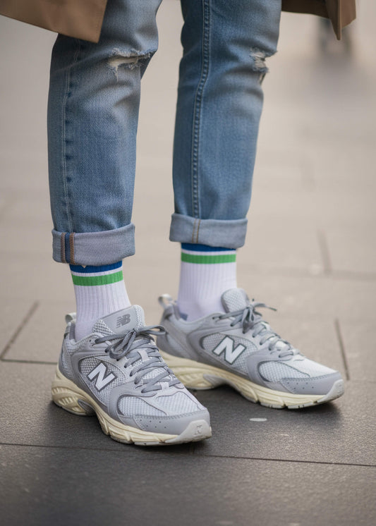 Eine Person mit blauer Jeanshose und New Balance Schuhen trägt die weißen Tennissocken mit blauen und grünen Streifen