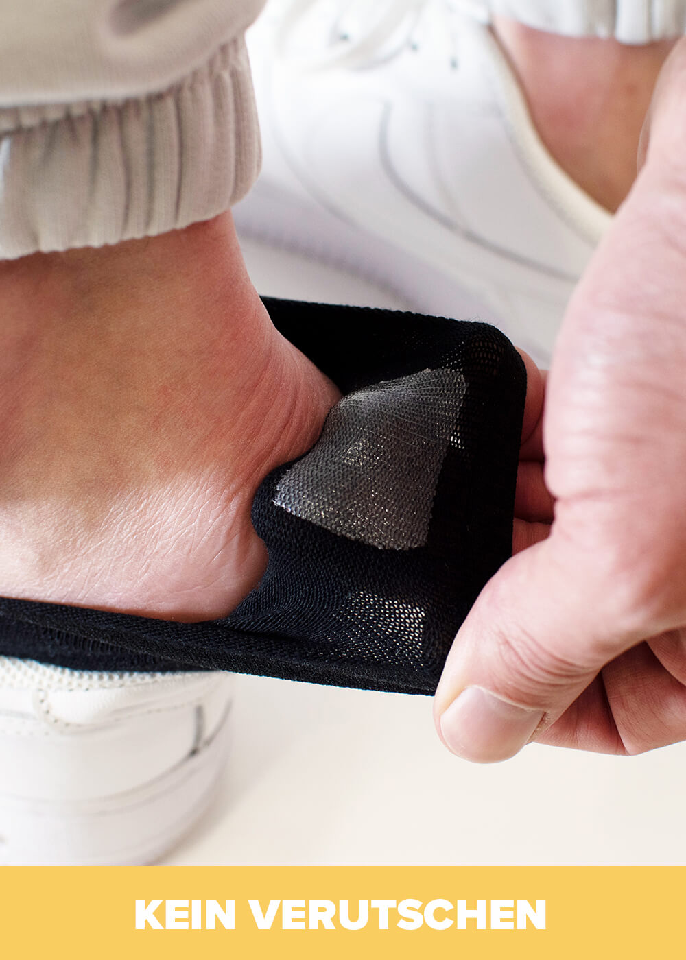 Eine Hand passt einen schwarzen Fersenschutz von J.Clay am Fußrücken eines weißen Sneakers an - perfekt für Füßlinge, die nicht rutschen. Unten steht in gelber Schrift KEIN VERUTSCHEN.